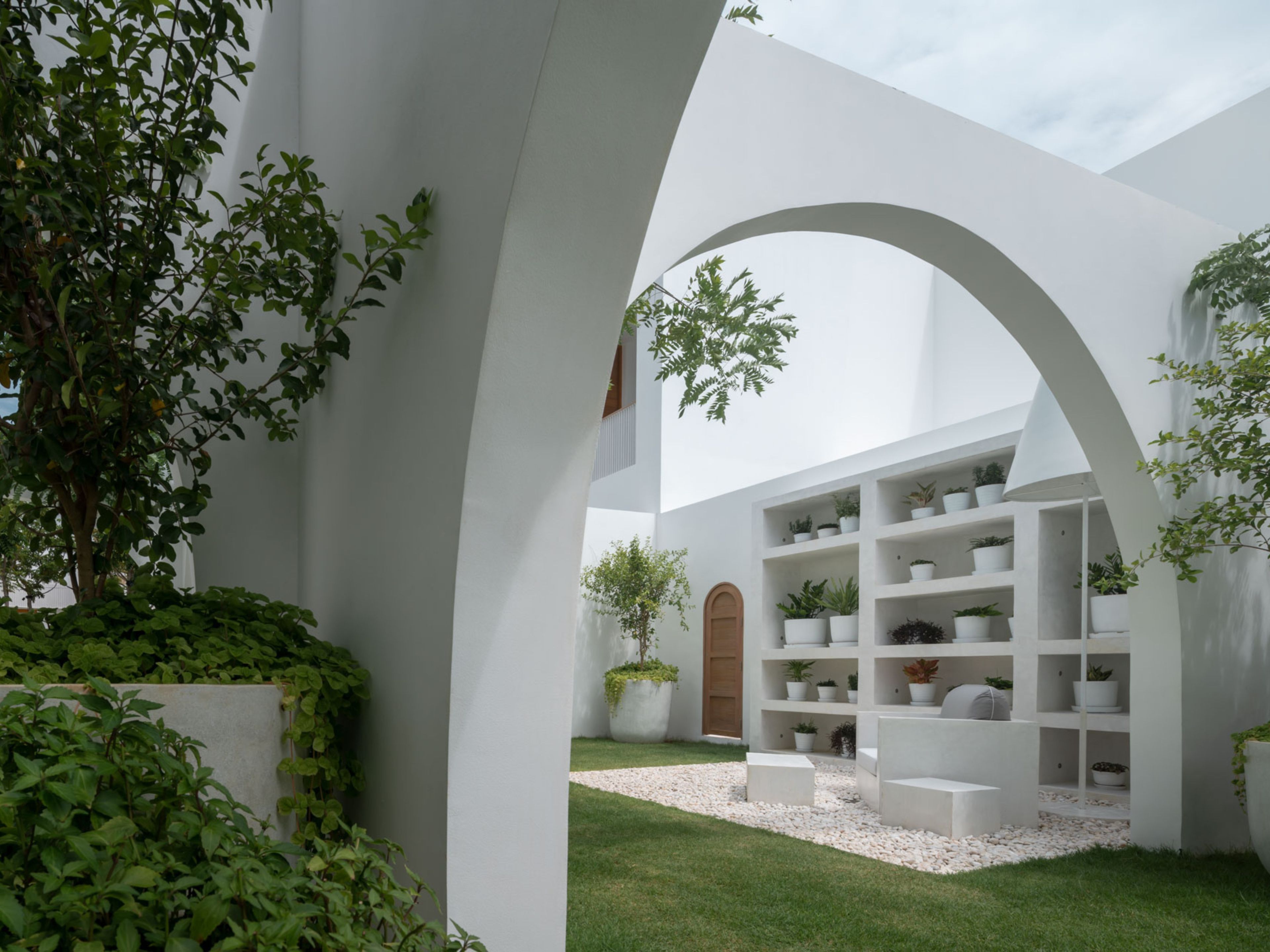 Un espace architectural moderne avec des murs blancs, une arche centrale et une collection de plantes en pot.