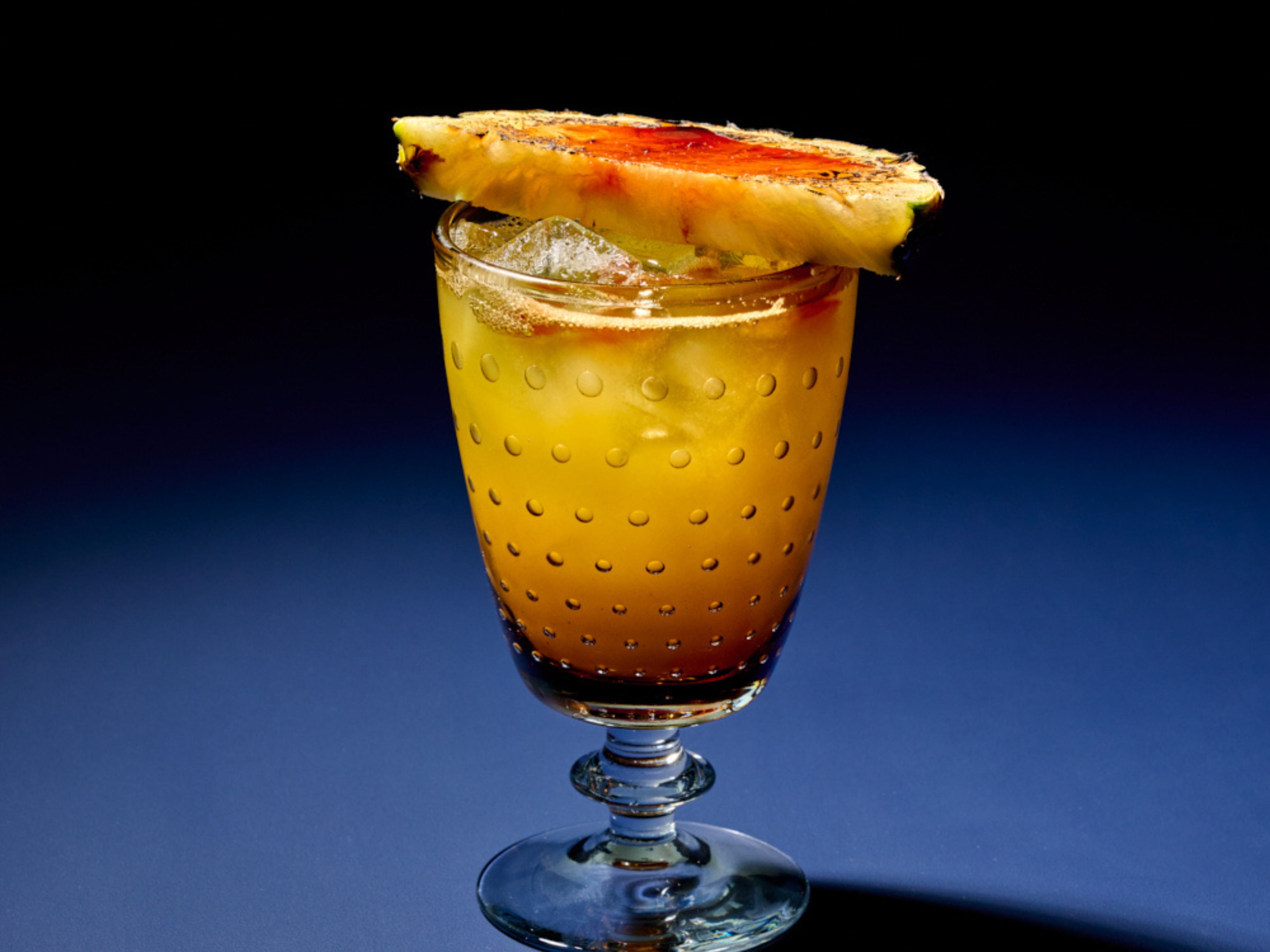 Un vaso de cóctel con una bebida en capas y una rodaja de fruta en el borde.
