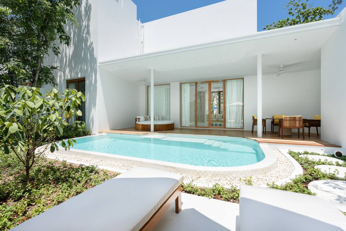 Un espace piscine extérieur moderne comprenant un coin détente avec des chaises longues, une table à manger avec des chaises et un petit coin salon avec des coussins.