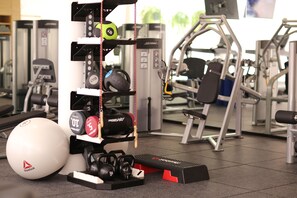 Un gimnasio con diversos equipos de ejercicio, como mancuernas, una pelota medicinal y discos de pesas.