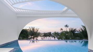 Vista despejada de una piscina con una estructura blanca curva en la parte superior, que refleja el cielo y palmeras circundantes.