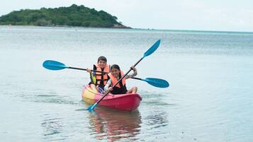 Two people in a kayak on calm water with a forested island in the background.