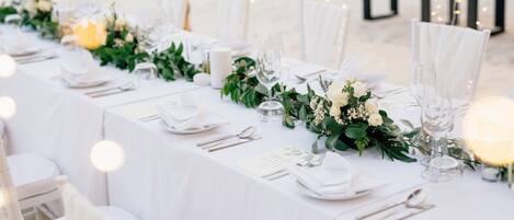 A beachside dining setup with white tablecloths, neatly arranged cutlery, and floral centerpieces.