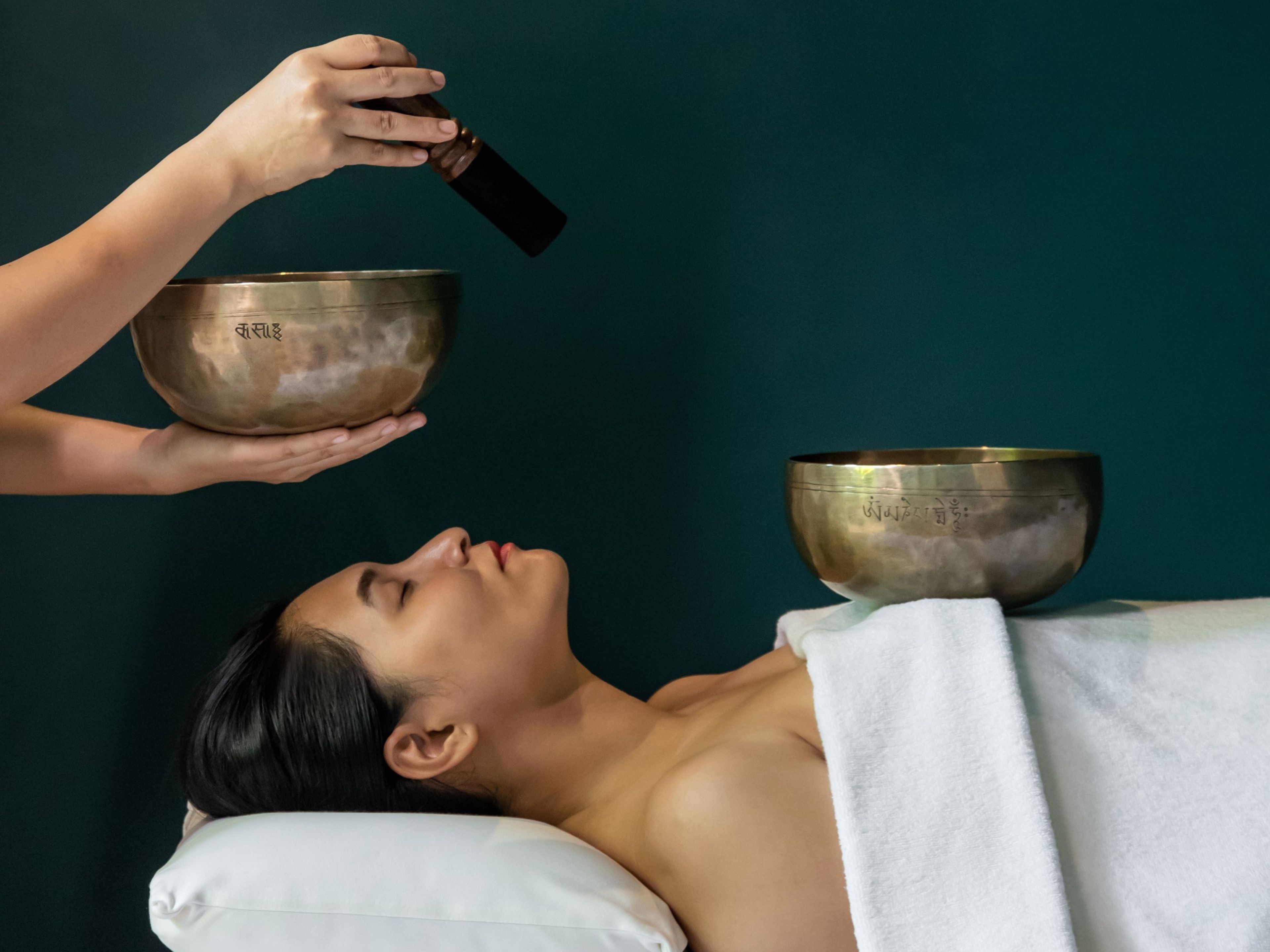 A person lying down with a bowl in front of them, another bowl held above, and a hand pouring something into the bowl.