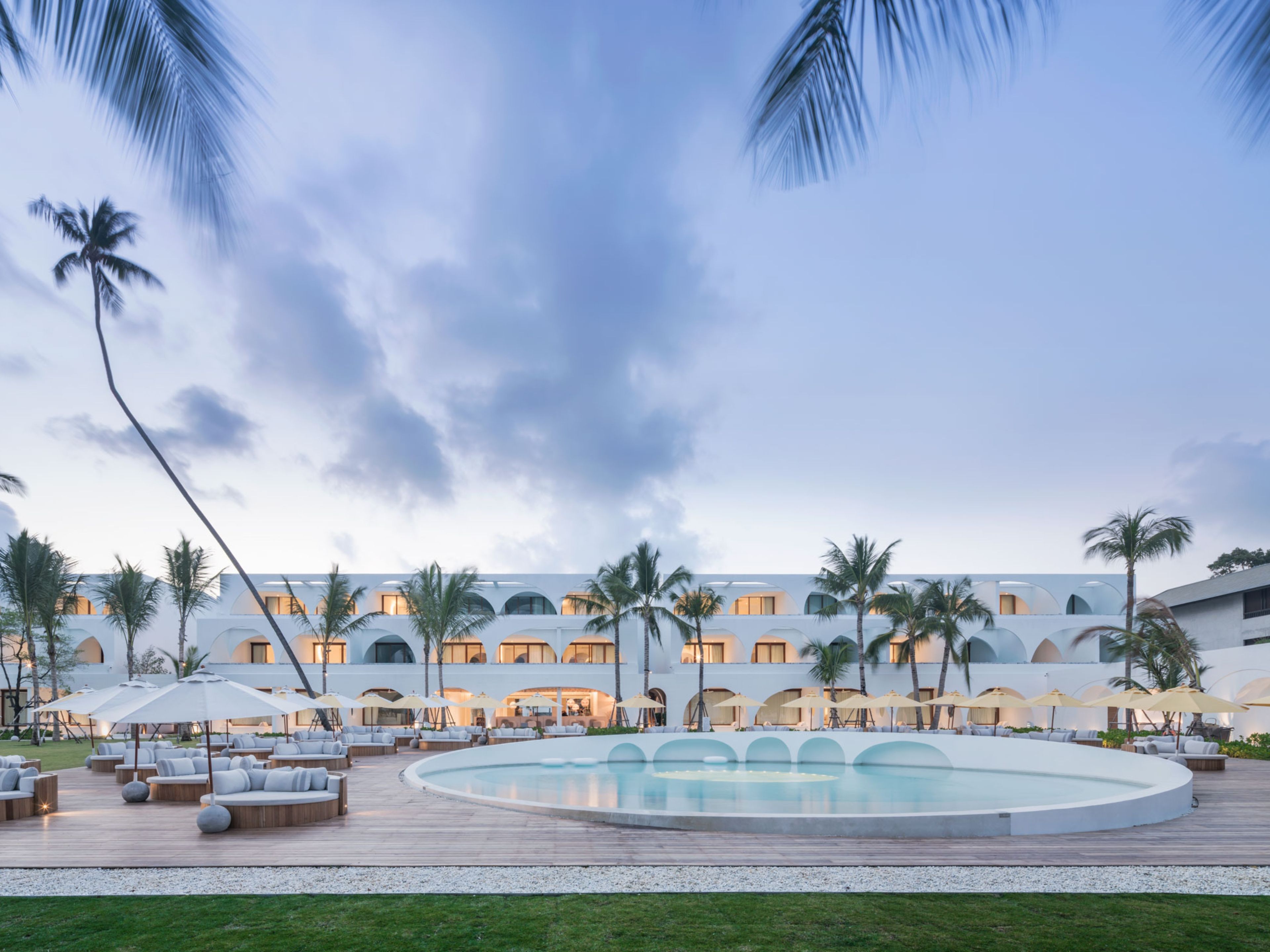 A resort with a pool, outdoor seating, palm trees, and a building with multiple balconies.