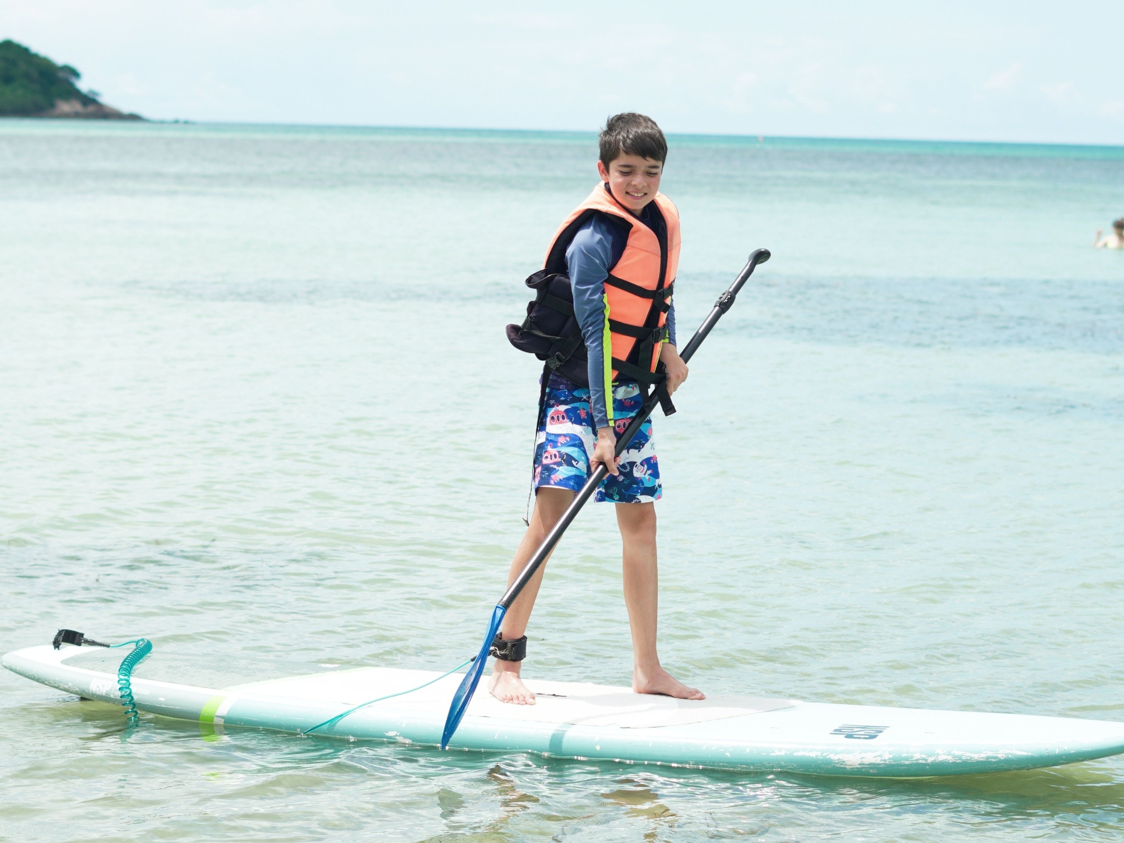 A person standing on a paddleboard in the water, wearing a life jacket and holding a paddle.