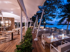 An outdoor dining area with tables and chairs, a wooden deck, and a view of the sea. - SALA Samui Chaweng Beach Resort (Koh Samui)