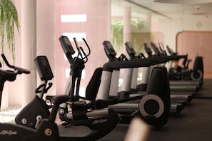 Varias bicicletas estáticas en un gimnasio con paredes blancas y un ventanal grande.