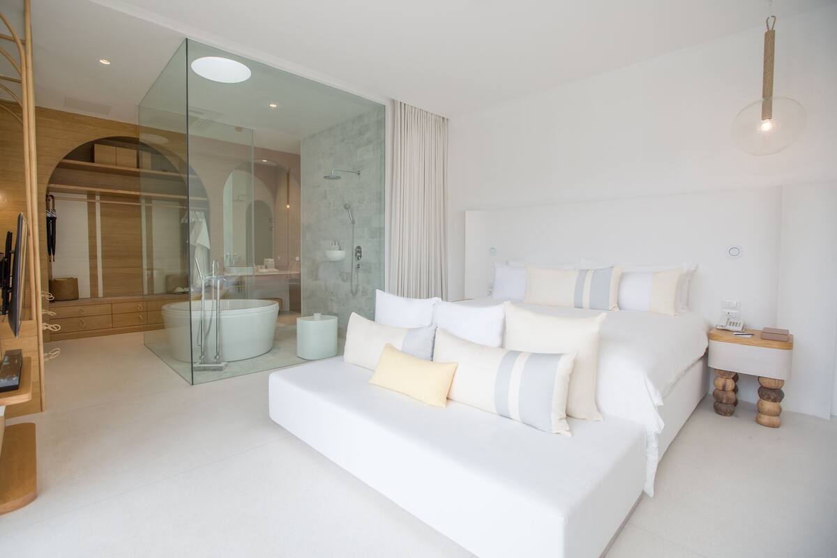 Une chambre à coucher moderne avec un grand lit, une douche en verre et une coiffeuse en bois.