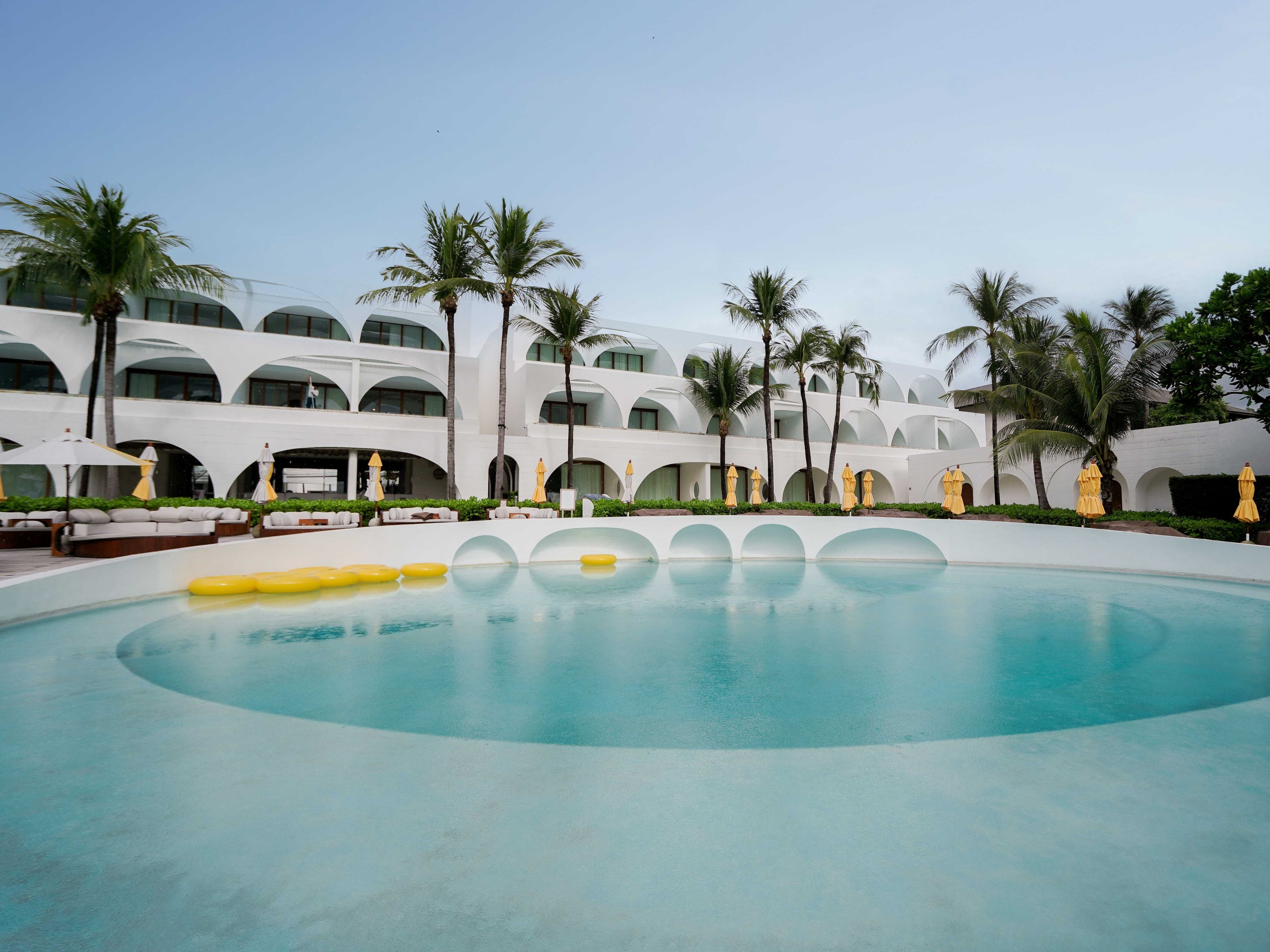 A hotel with a large pool, palm trees, and white architecture.