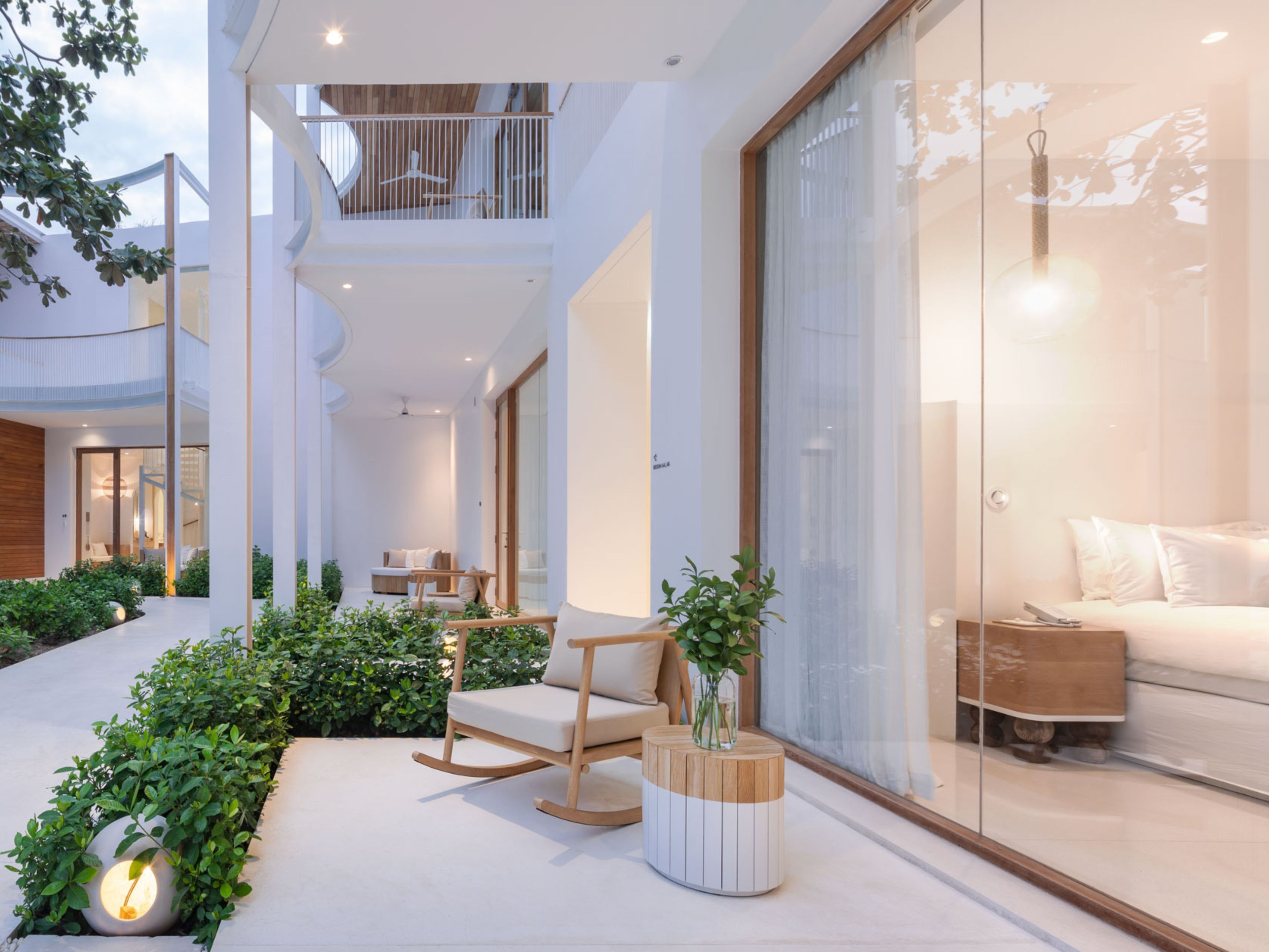 A modern hotel interior with a balcony, a seating area with a rocking chair, and a large window with a view.