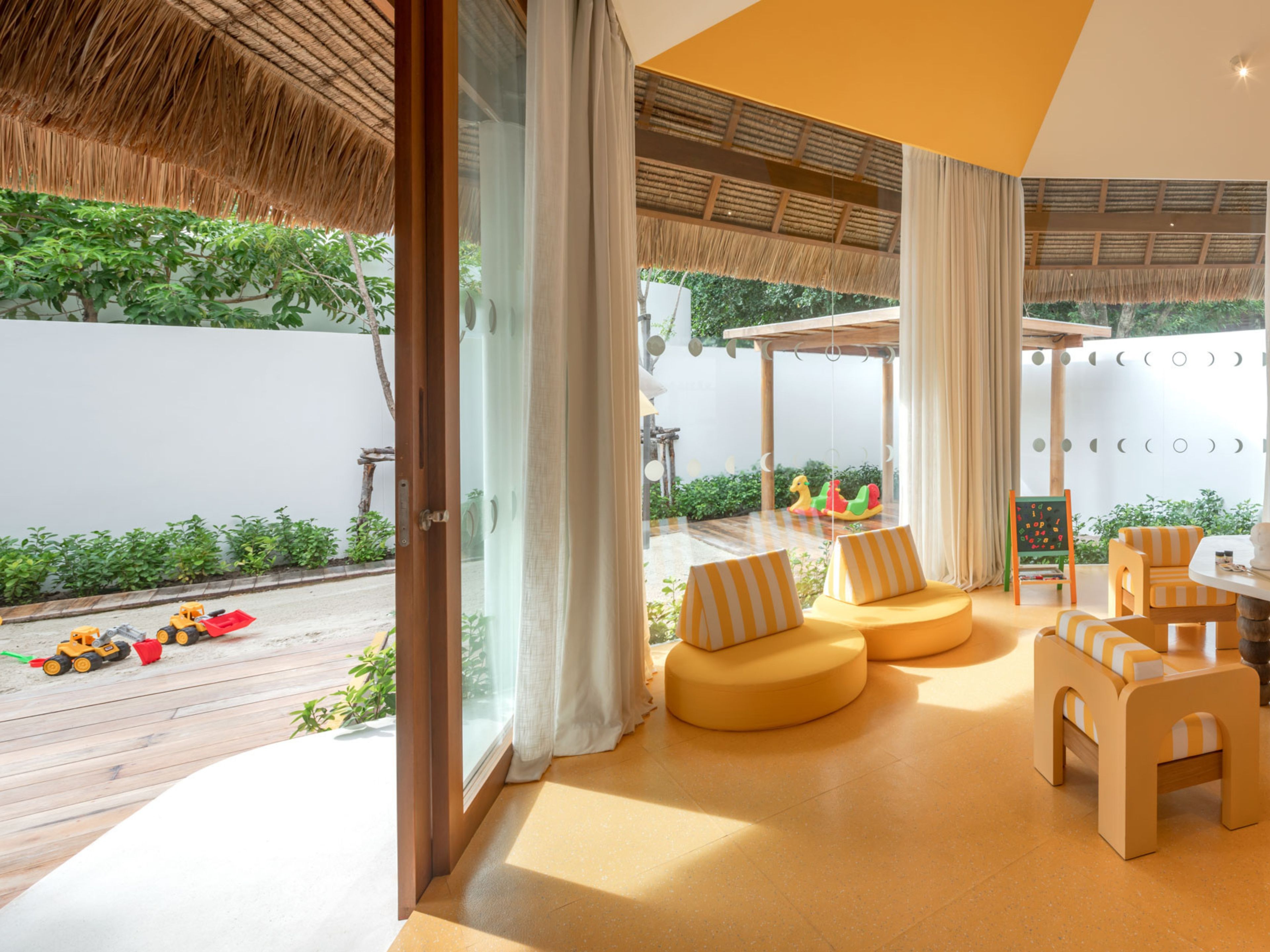 Een modern interieur met een grote glazen deur die uitkomt op een buitenruimte, met een houten terras en kinderspeelgoed.