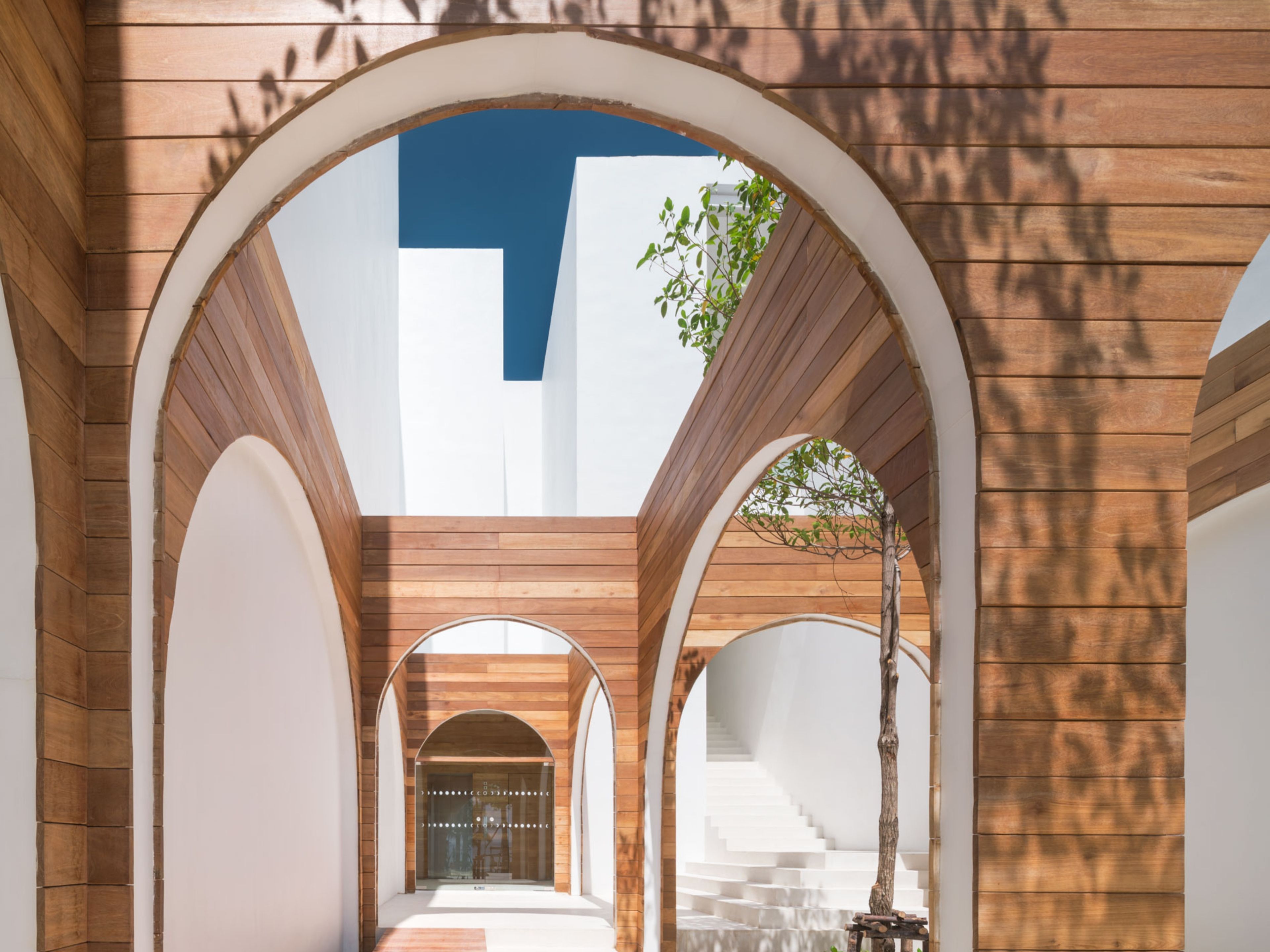 A corridor with wooden arches and a staircase leading to a white wall.
