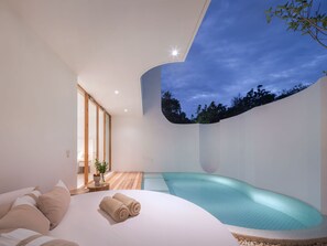 A modern bedroom with a large bed, a small pool, and a view of the sky.