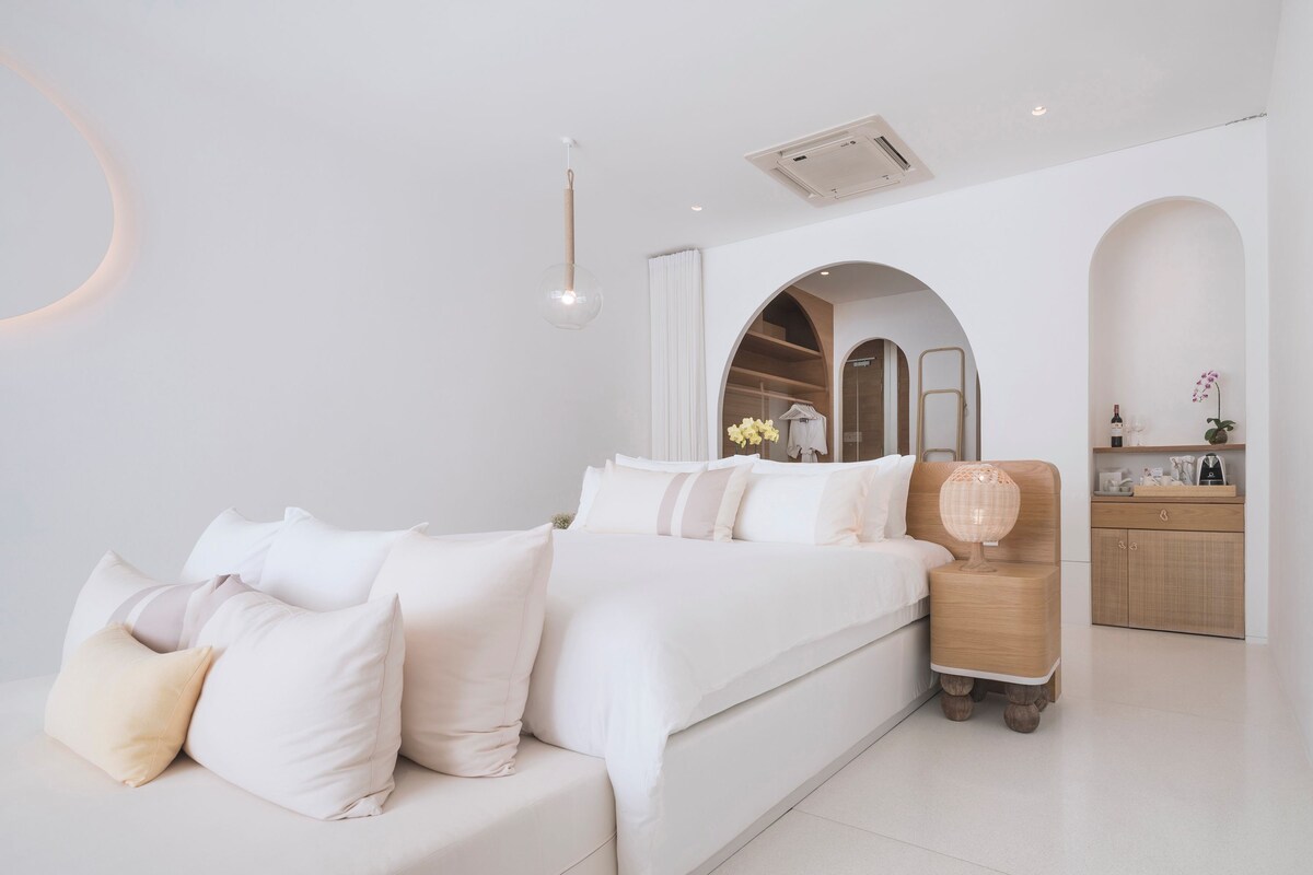 A modern bedroom with a large bed, a bedside table with a lamp, and a built-in wardrobe.