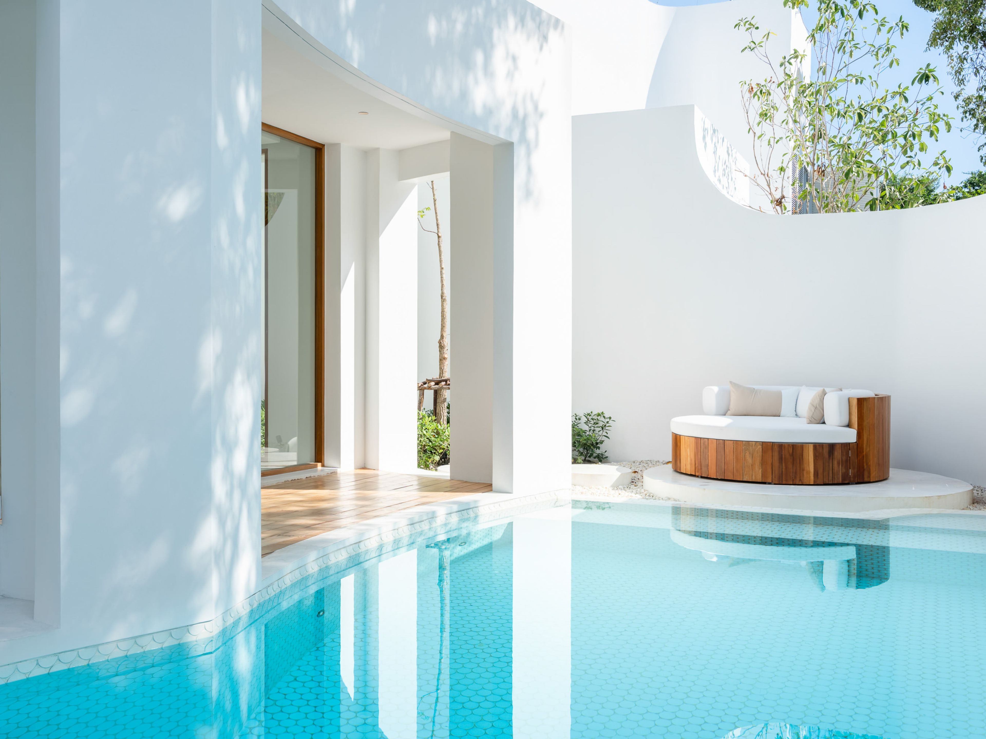 A modern pool area with a wooden deck, a white infinity pool, and a wooden bench with cushions.