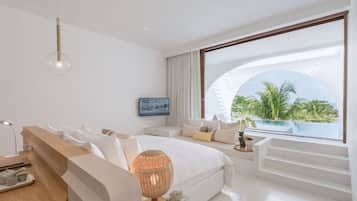 A modern hotel room with a large bed, a desk, and a view of the ocean.