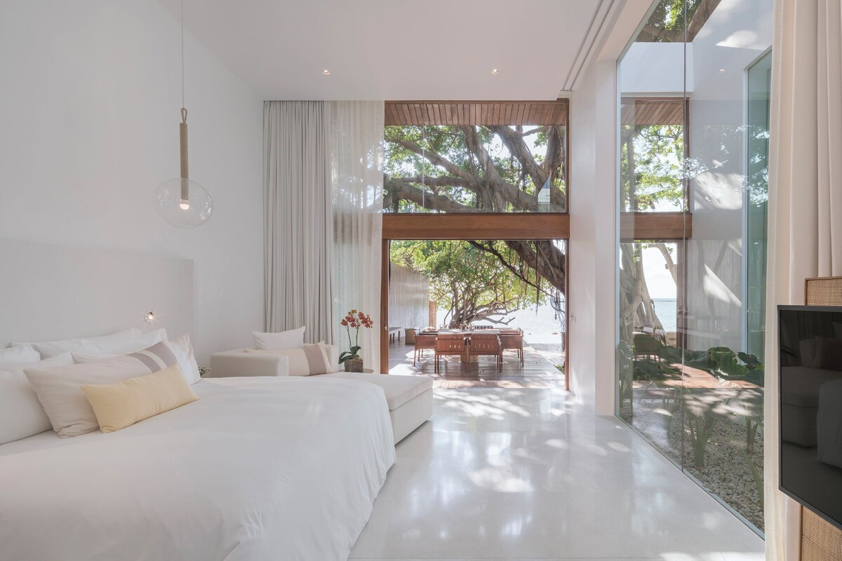 A modern bedroom with a large bed, a dining area, and a view of the outdoors.