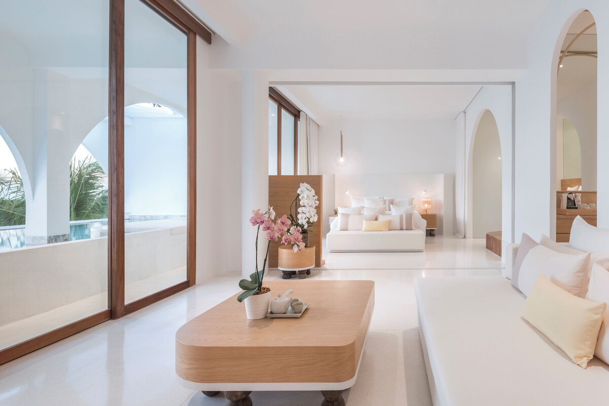 A modern hotel room with a large window, a wooden coffee table, a white sofa, and a wooden cabinet.