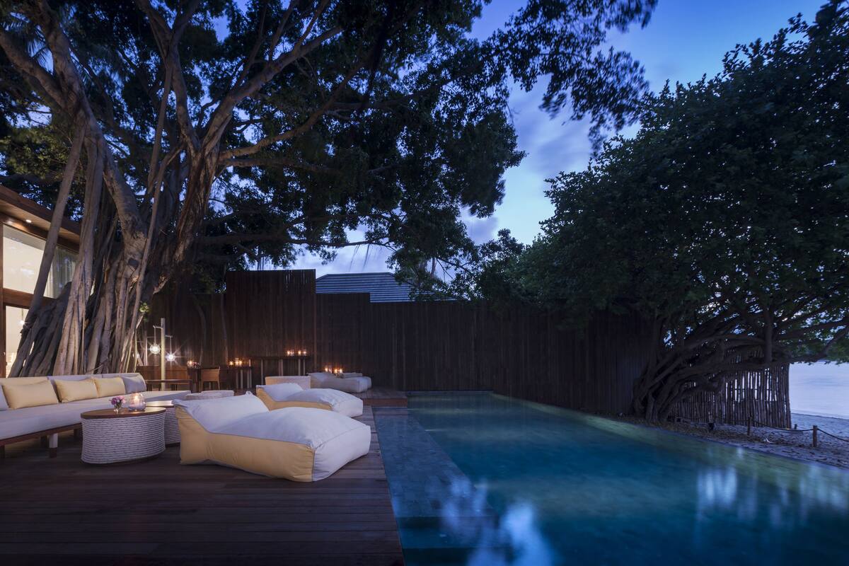 Un espace piscine extérieur paisible, doté d’une terrasse en bois, de chaises longues et offrant une vue sur l’eau.