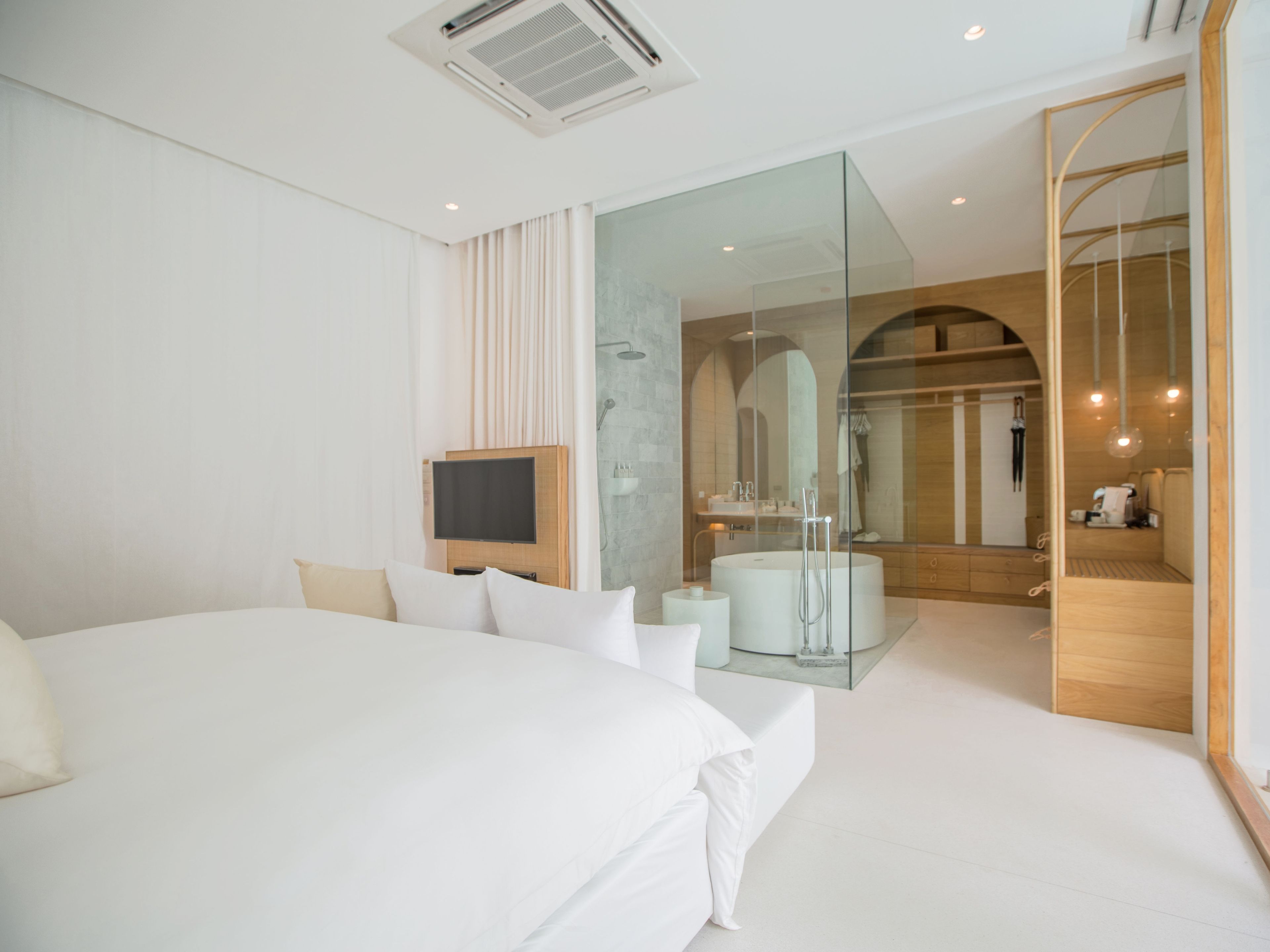 Una camera d'albergo moderna con un letto grande, una televisione, un angolo doccia in vetro e un comò in legno.