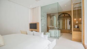 Una camera d'albergo moderna con un letto grande, una televisione, un angolo doccia in vetro e un comò in legno.