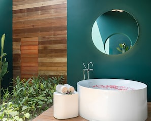 Un baño moderno con una bañera independiente, un espejo redondo y un revestimiento de pared de madera.