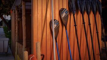 A row of paddles against a wooden wall, a rope, and a wooden structure with a rope ladder.