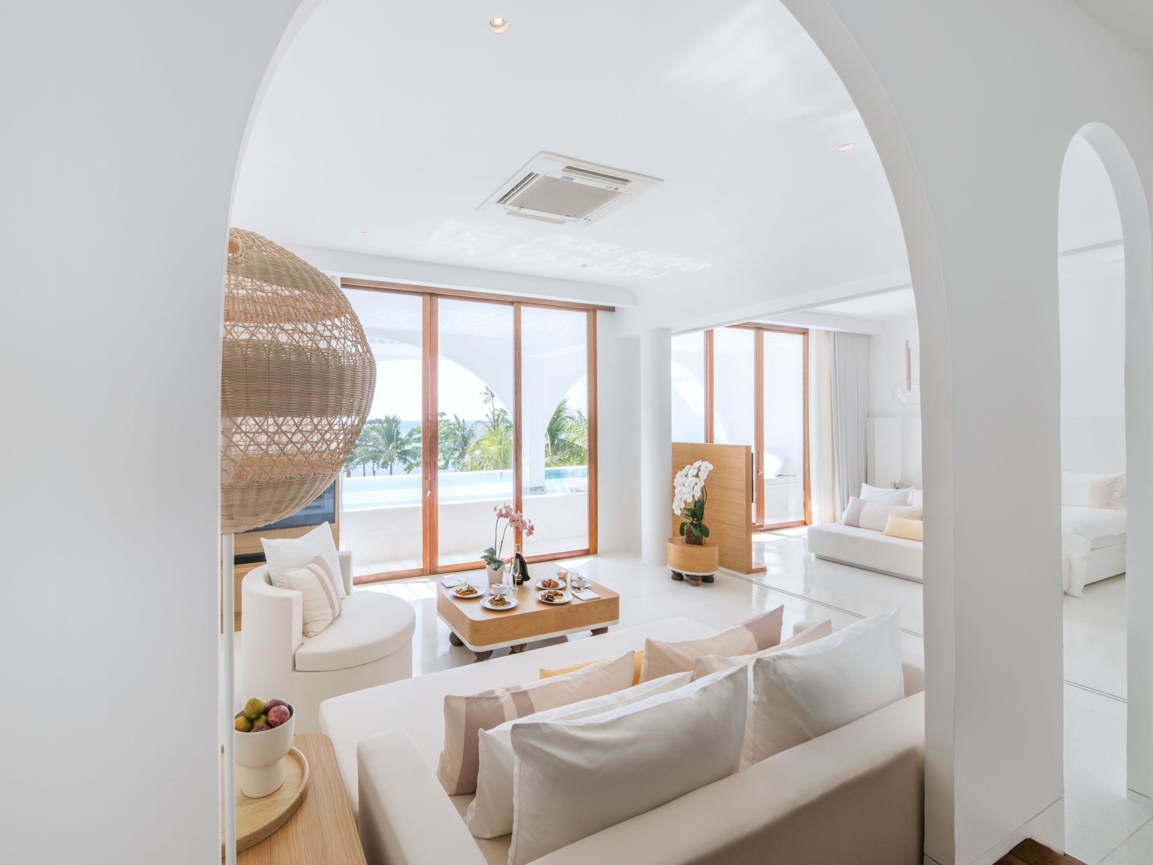A modern living room with a white sofa, a coffee table, and a wicker lamp.