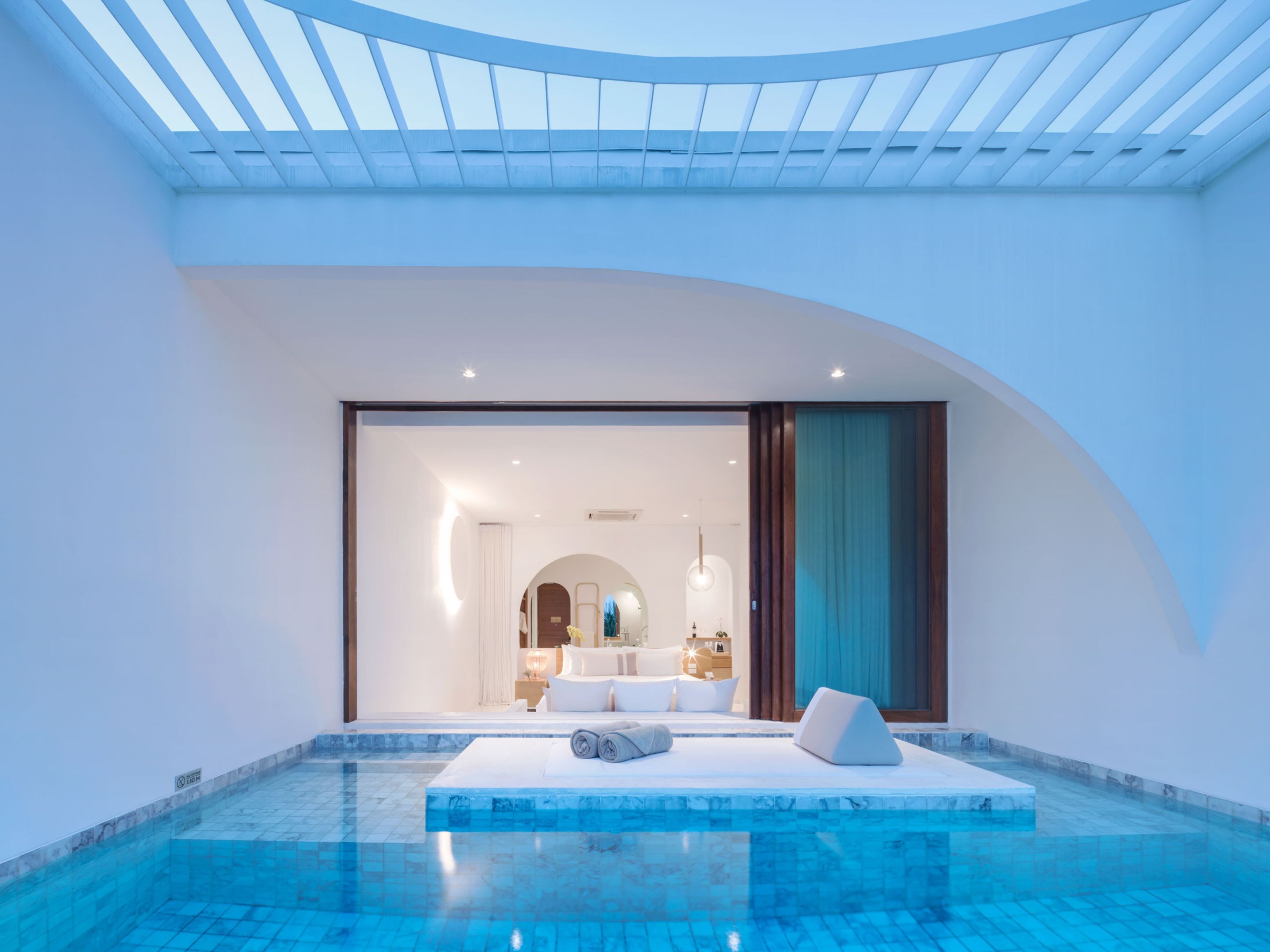 A modern indoor pool area with a clear view into a well-lit bedroom.