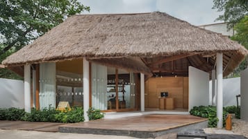 Un bâtiment moderne doté d’une entrée surmontée d’un toit de chaume, de planchers en bois et d’un espace détente avec des coussins.