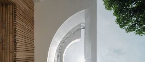 A modern architectural design with a curved white wall and a bamboo structure.