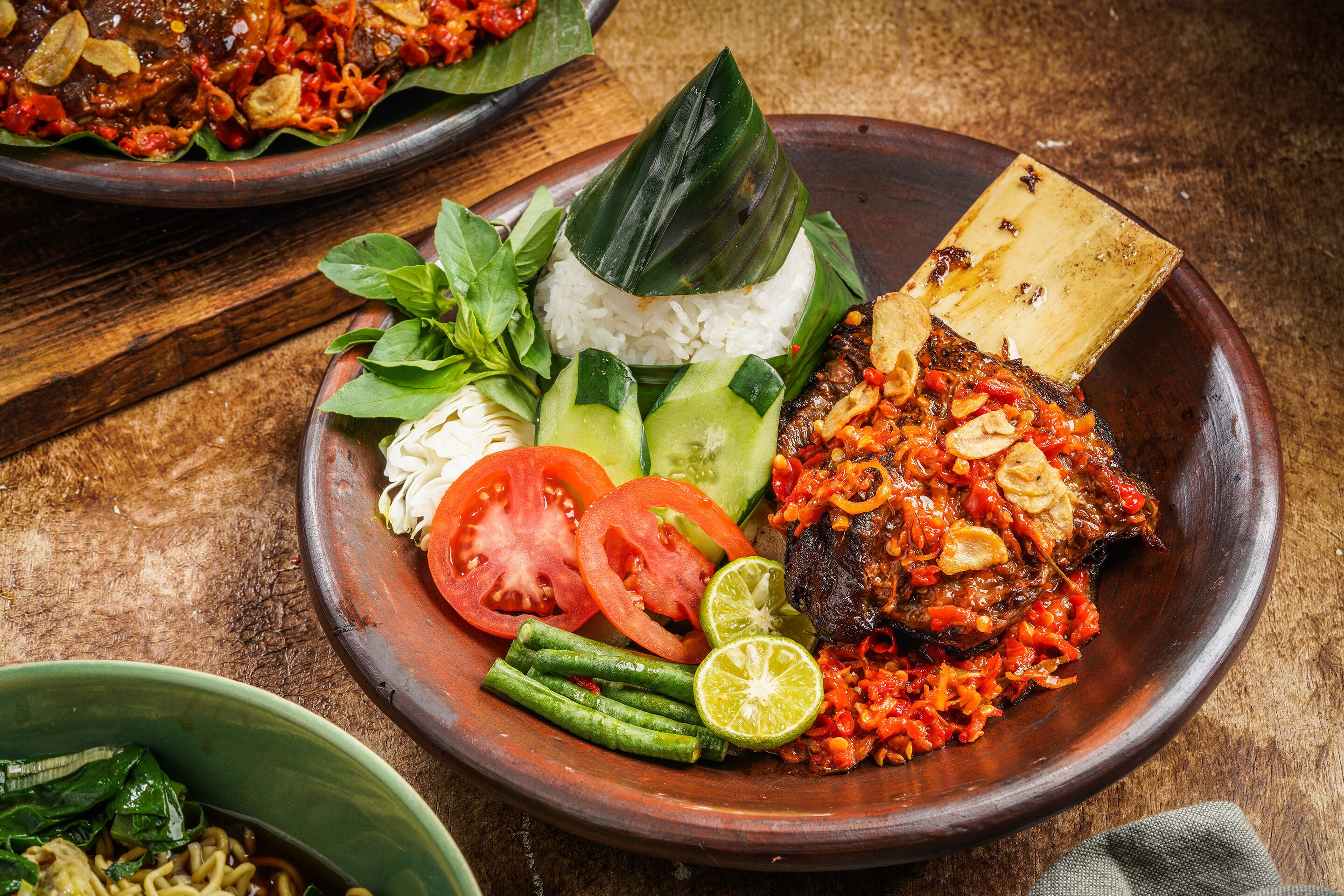 A meal with rice, vegetables, and grilled meat on a wooden plate.