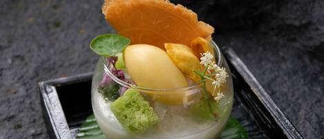 Un postre con un bol de vidrio, un plátano, una esponja verde y una hoja decorativa sobre una bandeja negra.