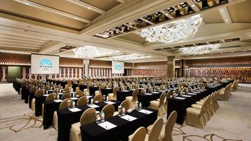 A conference room with rows of tables and chairs, a large screen, and a logo on the wall.