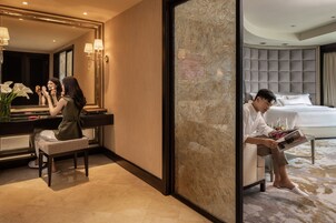 A hotel room with a large mirror, a vanity with a sink, a bed, and a reading area with a magazine.
