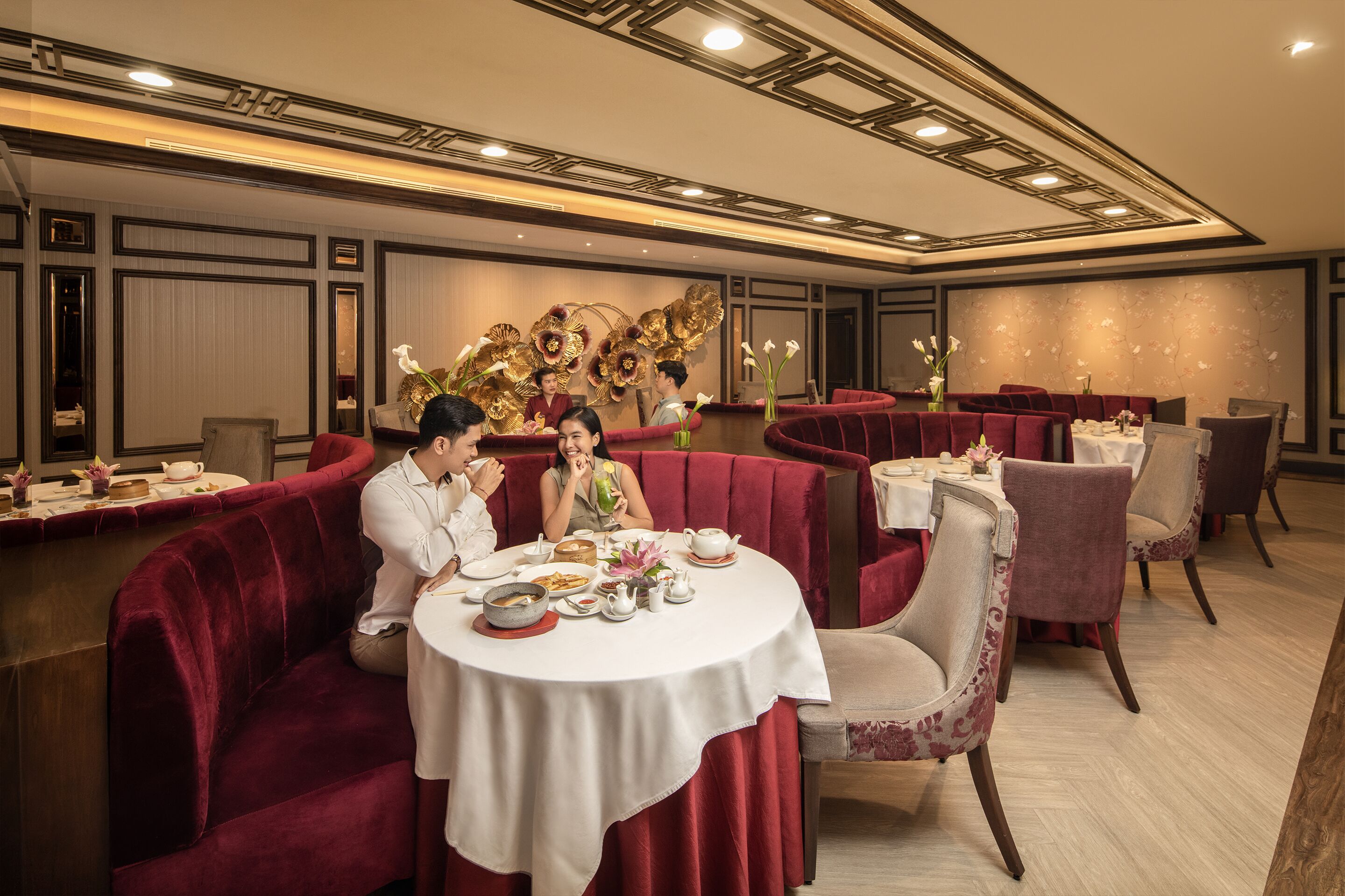 A restaurant with round tables, red velvet booths, and a decorative wall with floral patterns.