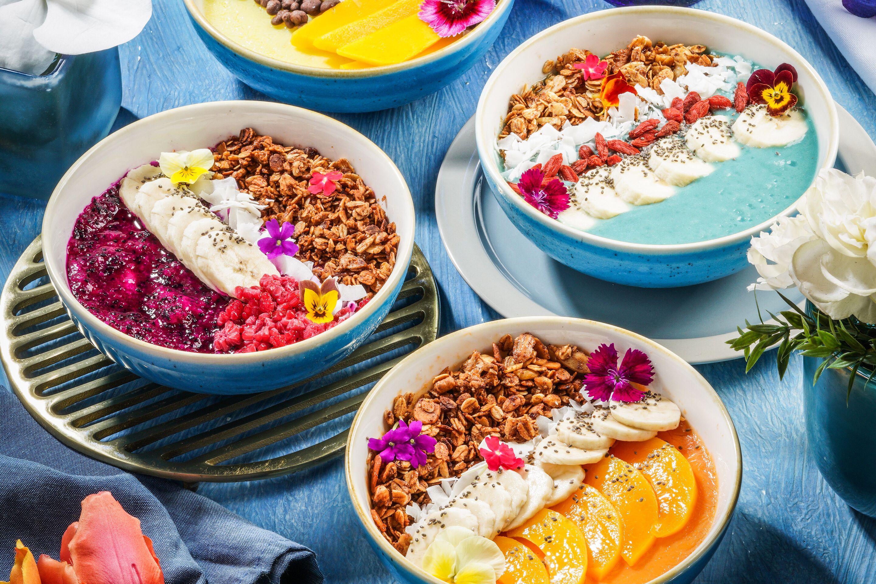 Three bowls of food with various toppings and fruits, placed on a blue wooden table.