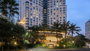 A modern hotel with a curved facade, surrounded by palm trees and well-lit by street lamps.