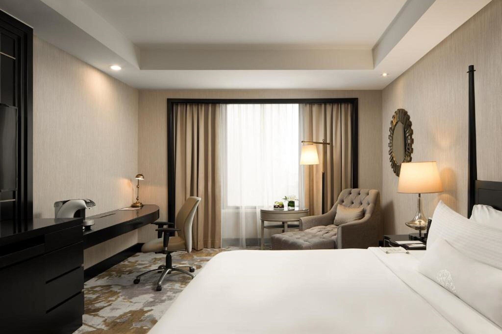 Habitación de hotel con cama, escritorio, silla, lámpara y vistas al exterior a través de la ventana.