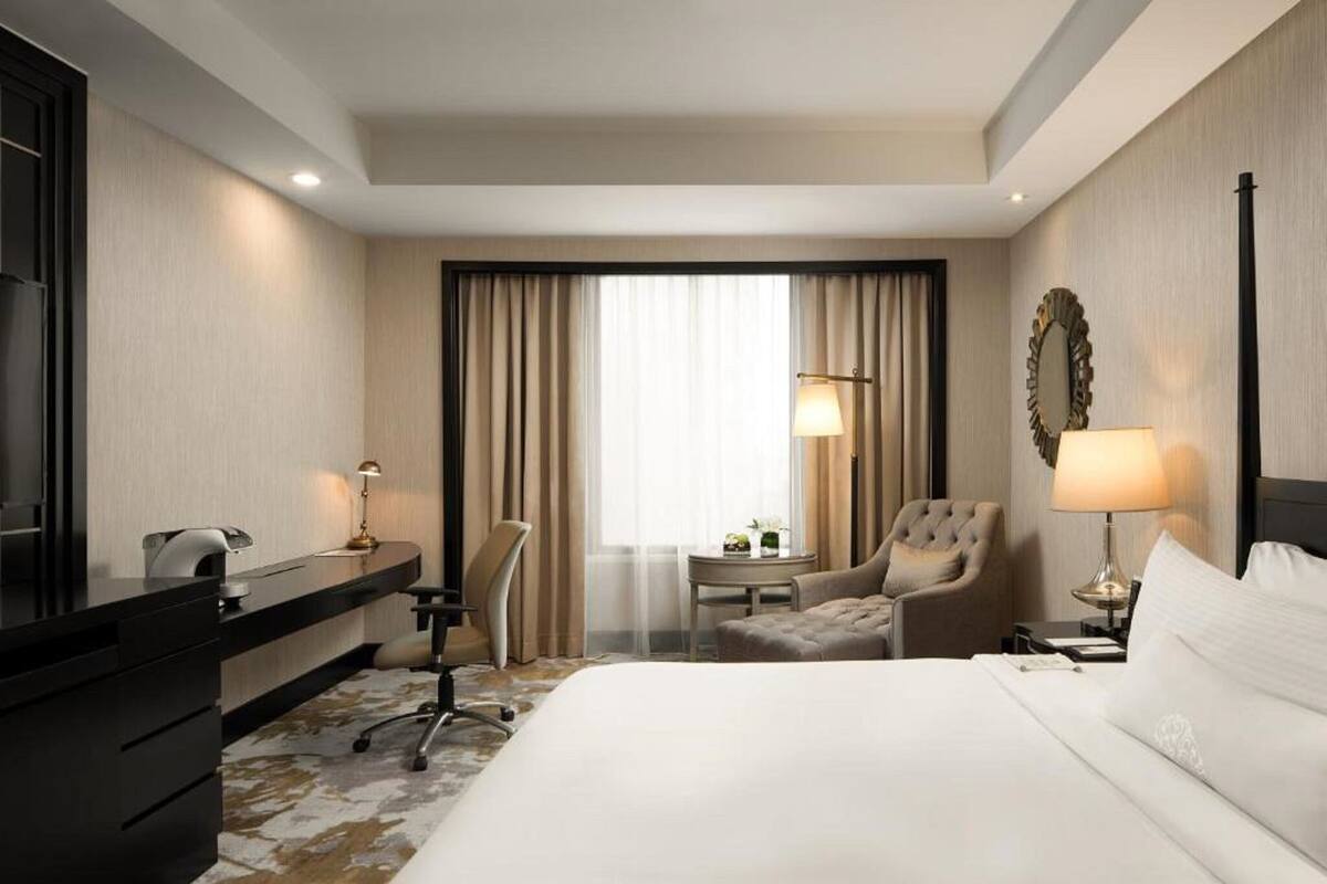 Habitación de hotel con cama, escritorio, silla, lámpara y vistas al exterior a través de la ventana.