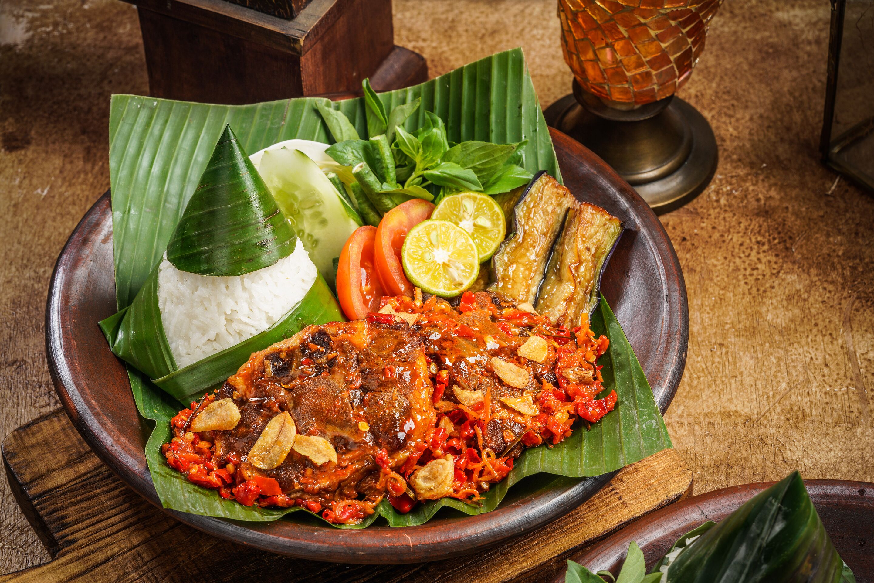 A traditional meal with rice, fish, and vegetables on a banana leaf, served on a wooden plate.
