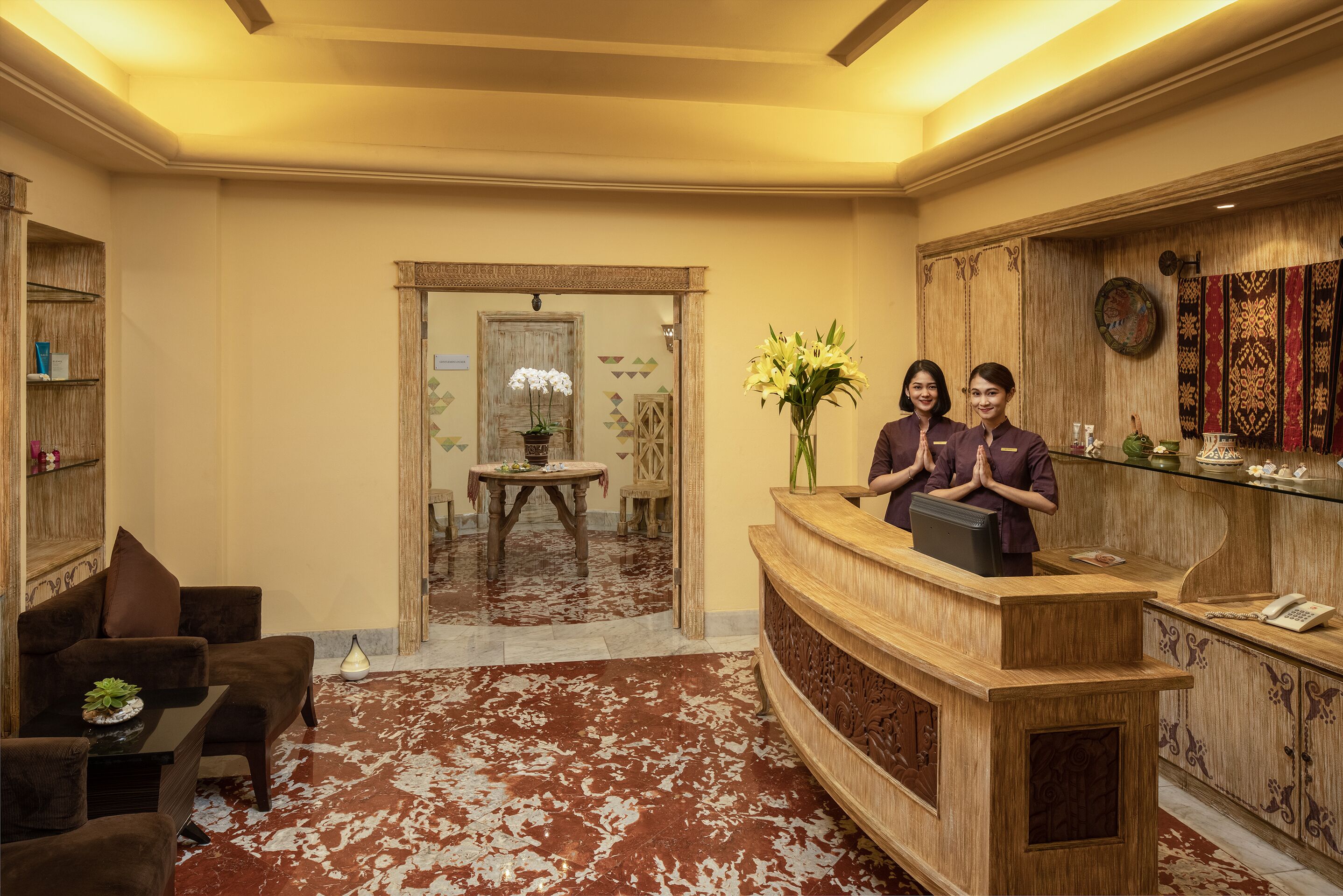 A reception area with a wooden desk, two receptionists, a floral arrangement, and a traditional decor style.