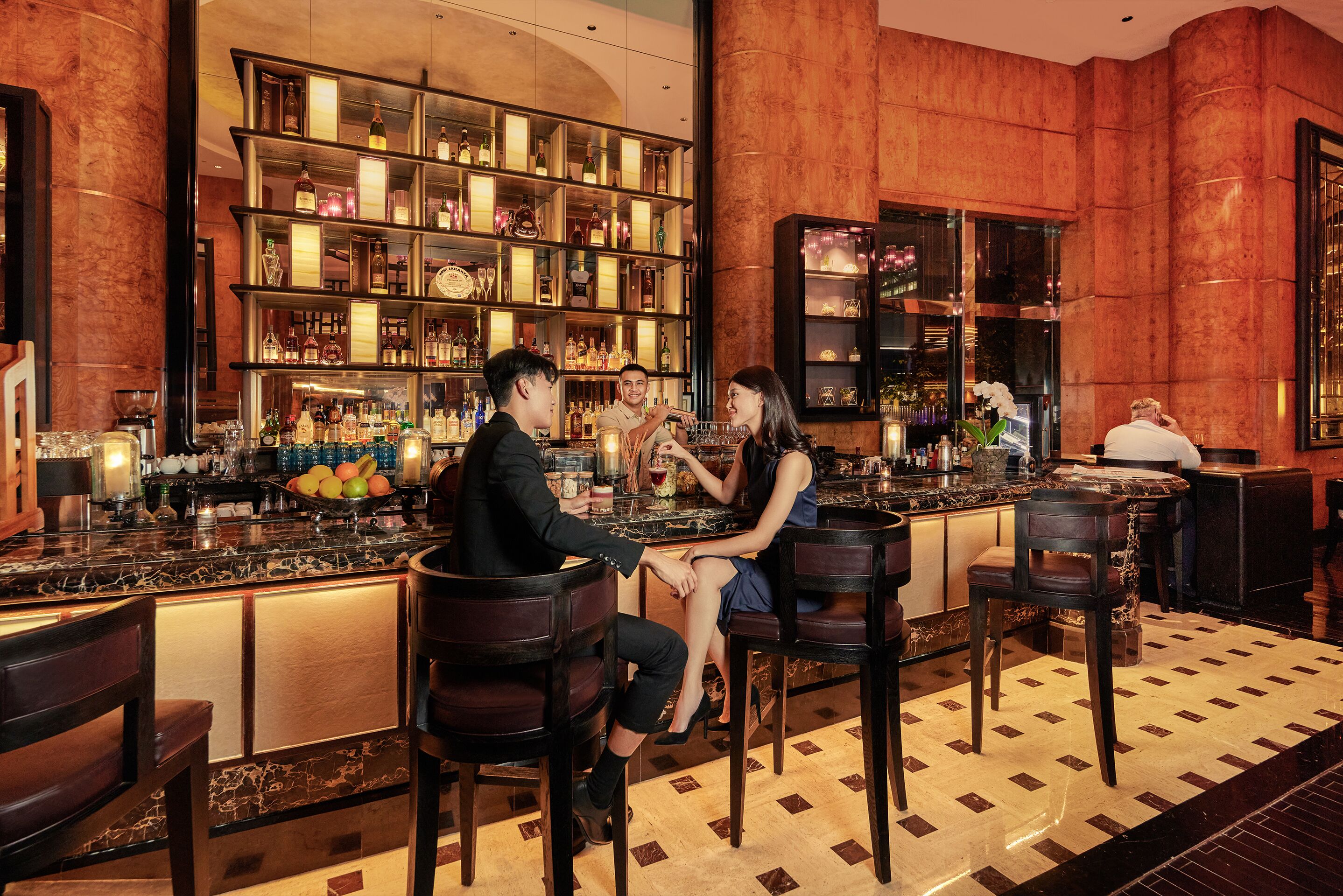 Una zona de bar con mostrador de mármol, varios taburetes y una estantería bien surtida con botellas y vasos.