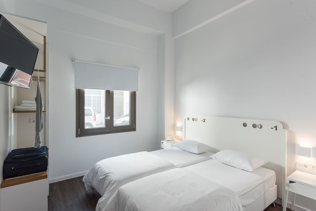 Ein Hotelzimmer mit zwei Betten, einem Fenster, einem Fernseher und einem Schreibtisch.