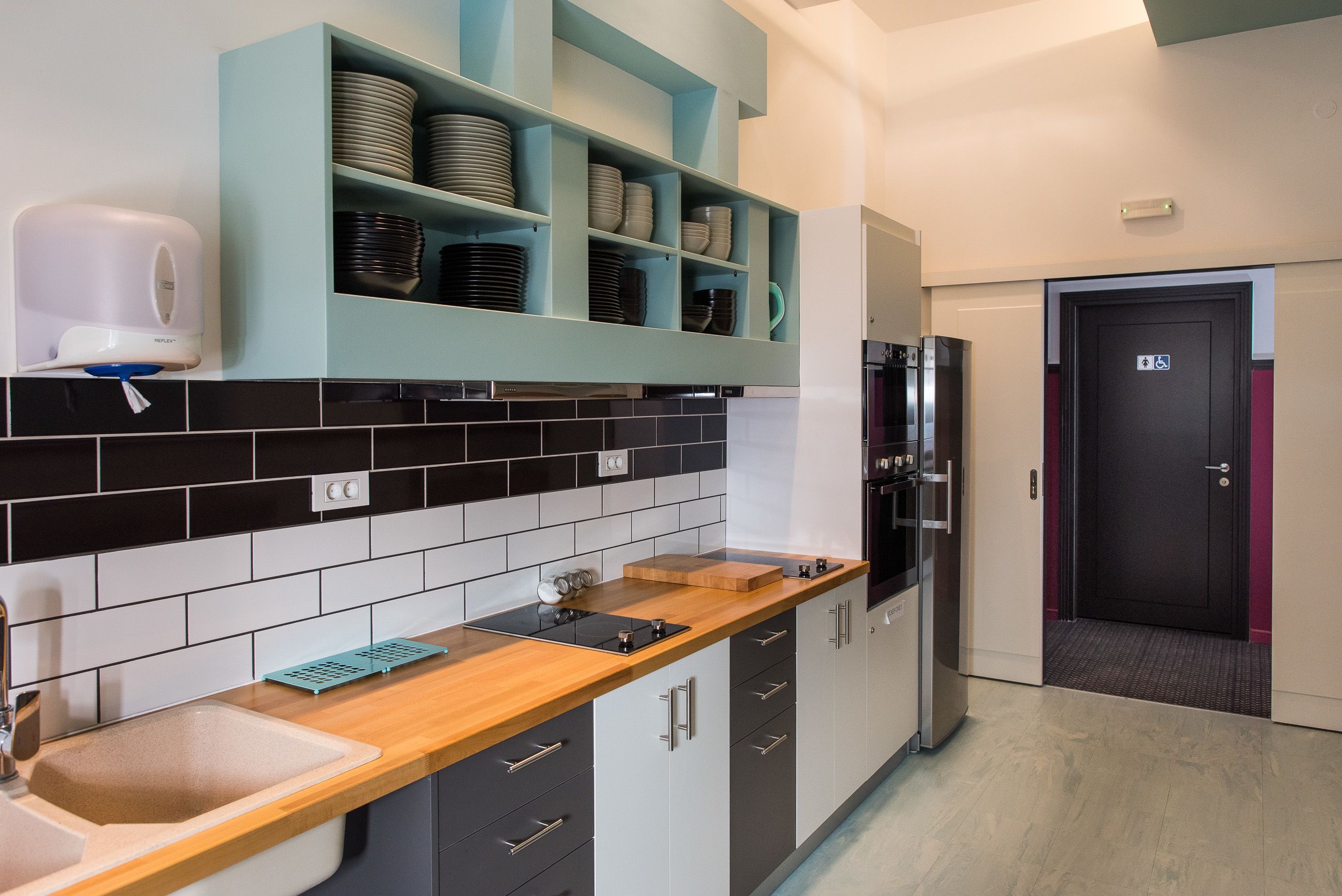 Una cucina moderna con zoccolo nero e bianco, un piano di lavoro in legno e mensole color acquamarina con piatti e ciotole.