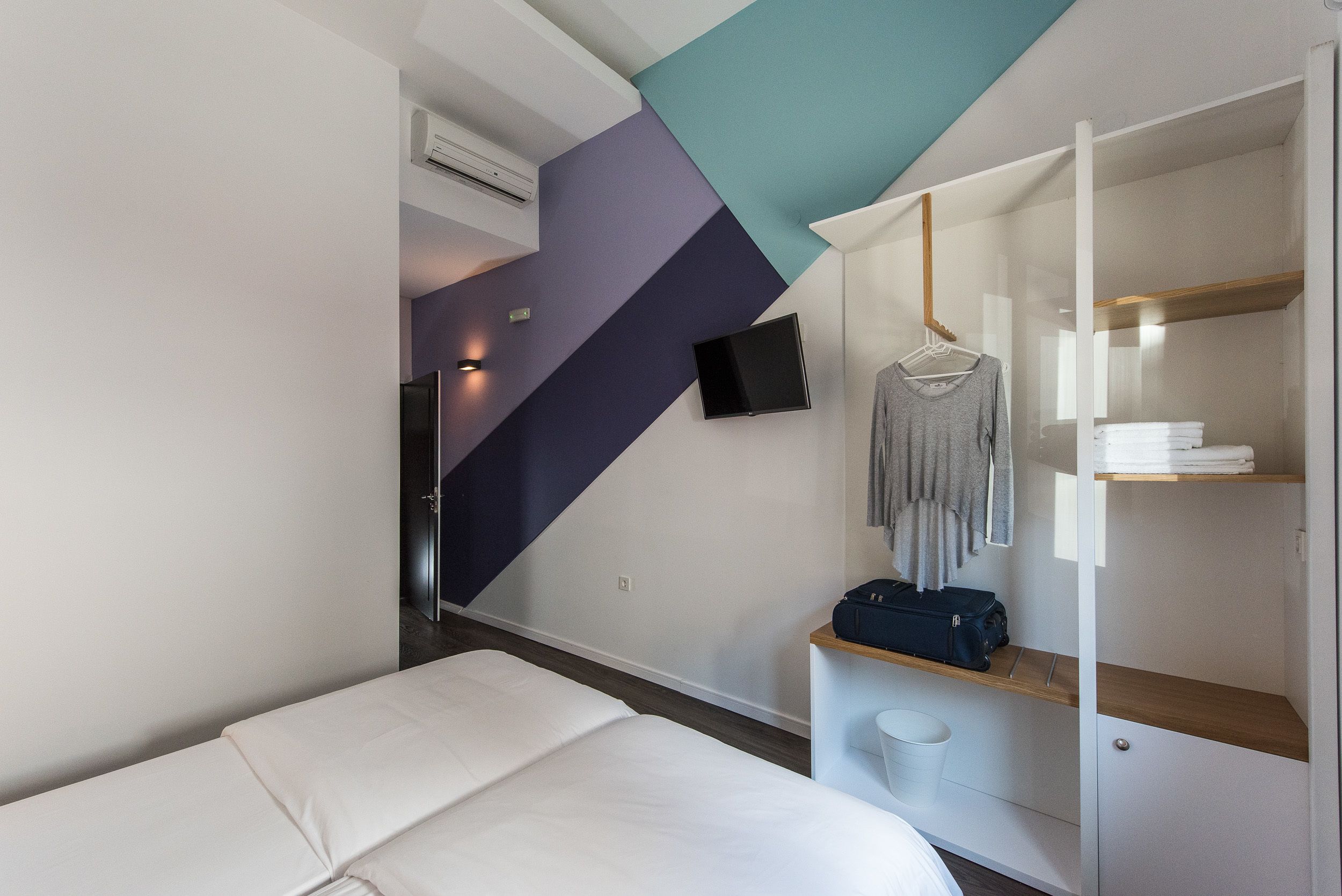 Ein modernes Hotelzimmer mit Bett, Schrank, Wand-Fernseher und einer kleinen Sitzecke.