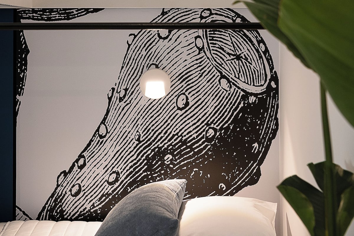 Ein Etagenbett mit Kopfteil, das ein schwarz-weißes abstraktes Design zeigt, ein Nachttisch und ein Blumentopf.