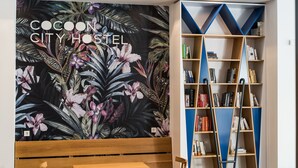 A cozy room with a wooden bench, a bookshelf, and a wall mural with tropical flowers. - Cocoon City Hostel (Chania)