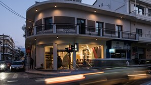A modern building with a curved facade, multiple balconies, and a ground-level entrance with a glass storefront. - Cocoon City Hostel (Chania)